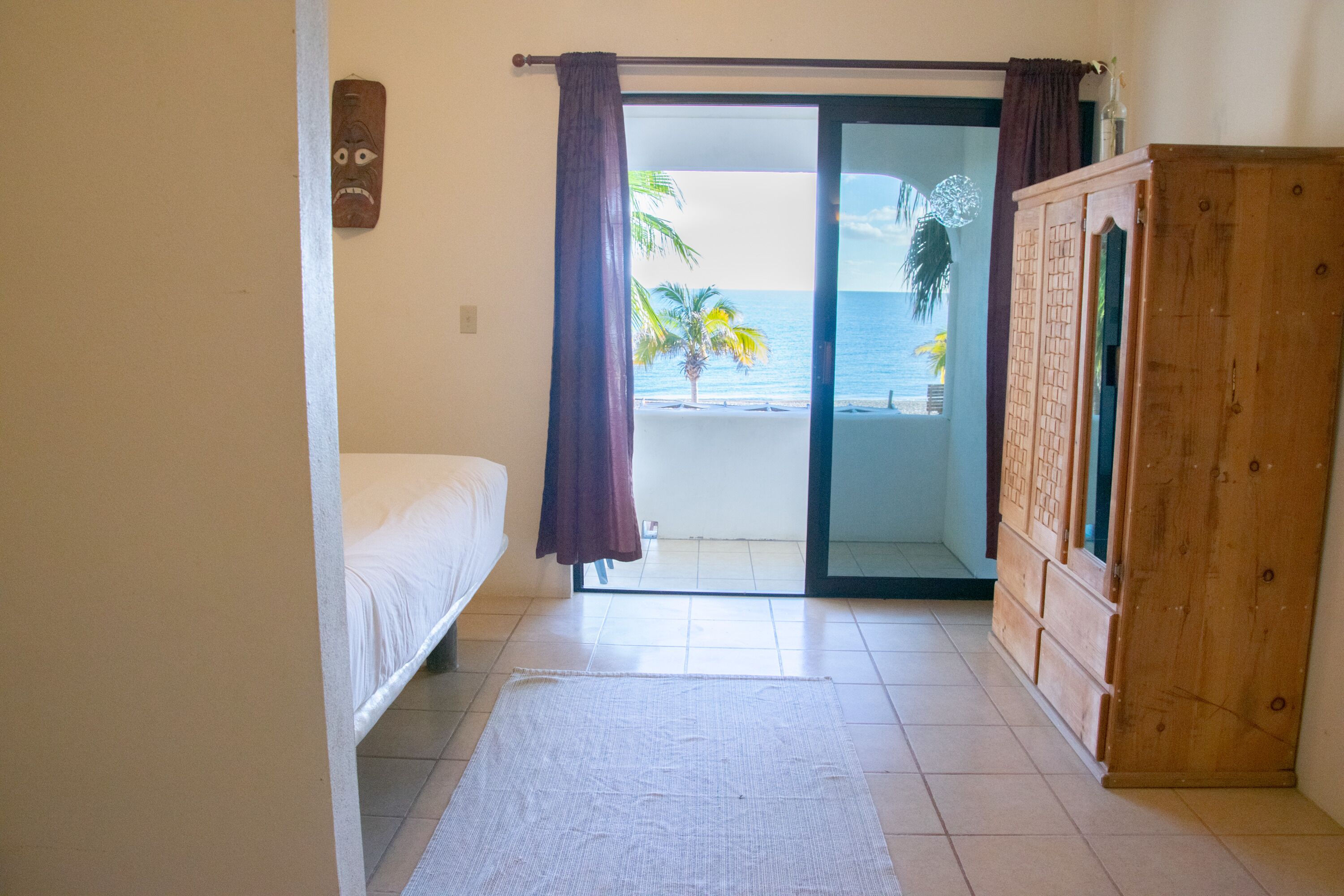 Een slaapkamer met een bed, een houten garderobe en uitzicht op het strand door een schuifdeur.