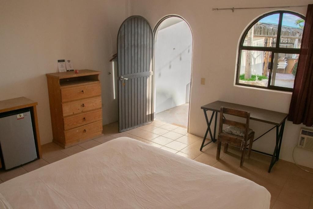 A bedroom with a bed, a wooden dresser, a desk with a chair, and a window with a view of the outside.