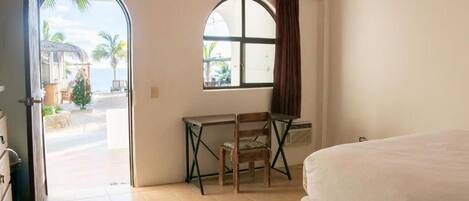 Una habitación con cama, escritorio y silla, ventana con cortinas y vista a la playa.