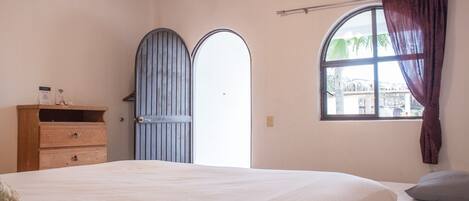 Un dormitorio con una cama grande, un aparador de madera, una ventana con cortinas y una puerta con reja de metal.