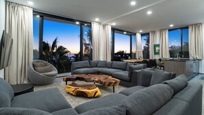 A modern living room with grey sofas, a unique wooden coffee table, and large windows offering a view of palm trees and the ocean. - La Ventana Beach Resort (La Ventana)
