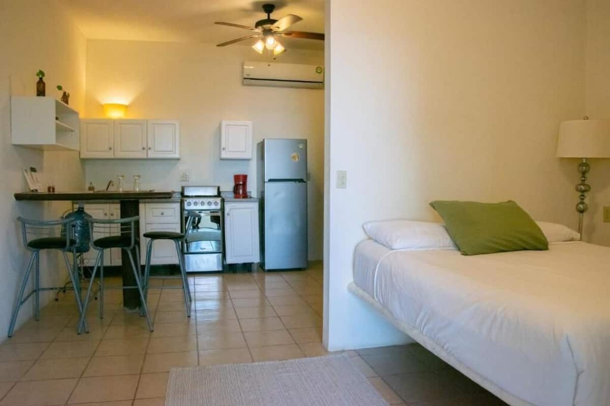 Une petite chambre comprenant un lit, un coin cuisine et un ventilateur de plafond.