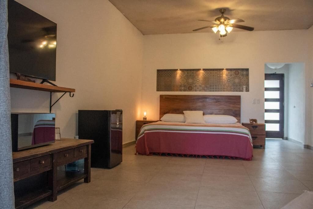 A bedroom with a bed, a television, a ceiling fan, and a wooden headboard.