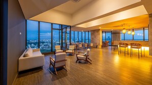 A spacious lounge area with a high ceiling, large windows offering a city view, and a bar area with seating. - Oceanview 20th Fl/Rooftop Pool/Gym/Historic Center (Cartagena de Indias)