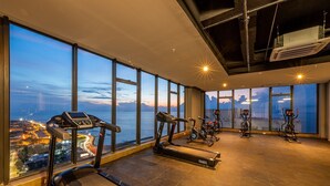 A gym with treadmills, stationary bikes, and a rowing machine, large windows with a city view, and a high ceiling with exposed beams and an air conditioning unit. - Oceanview 20th Fl/Rooftop Pool/Gym/Historic Center (Cartagena de Indias)