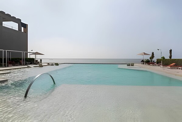 A swimming pool with a clear view of the sea, a covered seating area, and a building with a modern design.