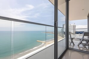 A balcony with a glass railing overlooking a beach and the sea.