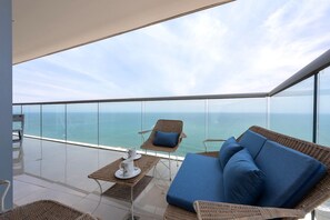 A balcony with wicker furniture, a table with a cup and saucer, and a view of the ocean.