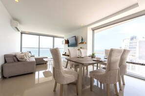 A modern living room with a dining area, large windows, and a view of the city.