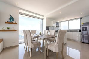 A modern kitchen with a built-in refrigerator, a dining area with a round table and chairs, and a view of the city through large windows.