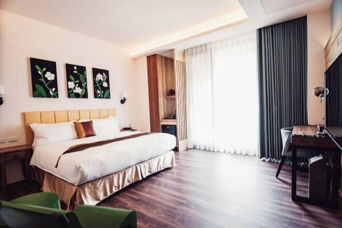 Et hotelværelse med seng, skrivebord, stol og billedkunst på væggen.