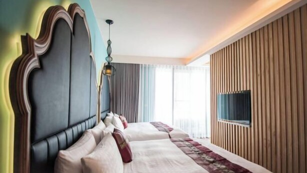 A hotel room with a large bed, a headboard, a television, and a window with curtains. - Dreamer Boutique Hotel (Pingtung)