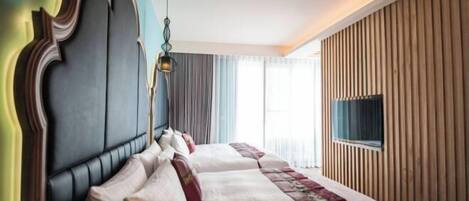 A hotel room with a large bed, a headboard, a television, and a window with curtains.