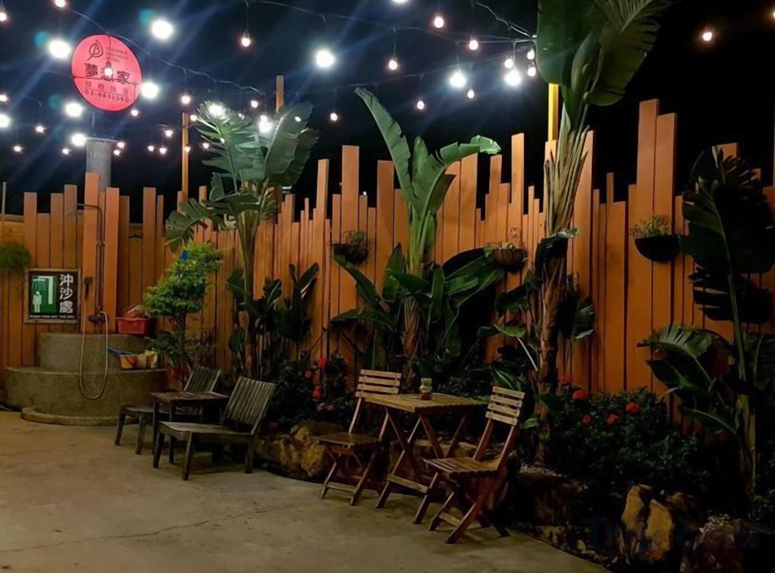 Un espace extérieur aménagé avec des chaises et des tables en bois, entouré de plantes tropicales et délimité par une clôture en bois.