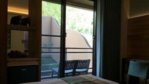 A bedroom with a bed, a desk, and a chair. There is a window with a view of a wooden fence and greenery outside. - Dreamer Boutique Hotel (Pingtung)