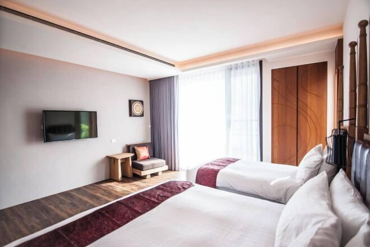 Et hotelværelse med to senge, et fjernsyn, et lille bord og et vindue med gardiner.