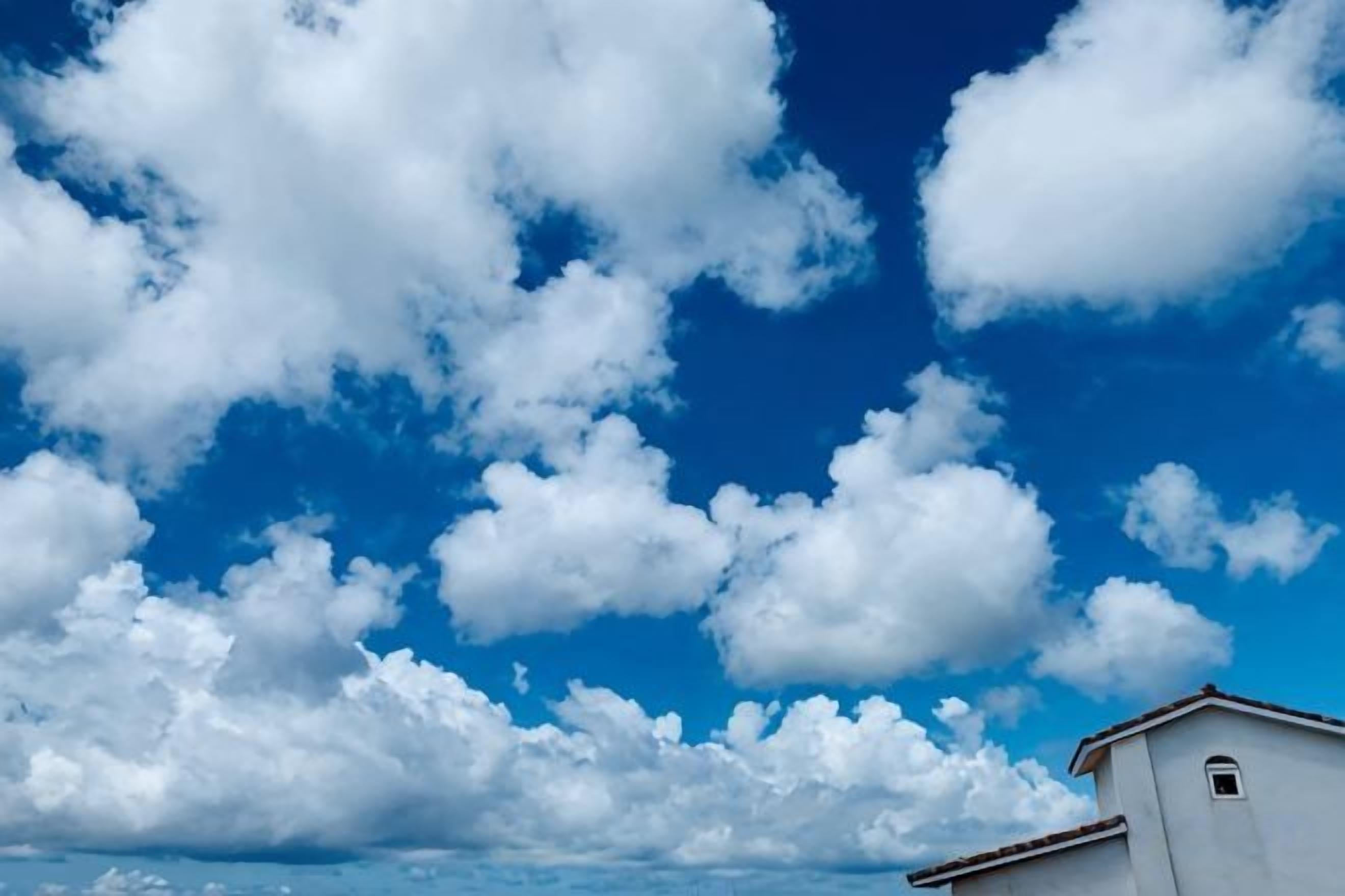 A clear blue sky with scattered clouds and a building with a white facade and red roof.