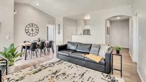 Ein modernes Wohnzimmer mit einem schwarzen Ledersofa, einem Esstisch mit Stühlen und einer großen Wanduhr.