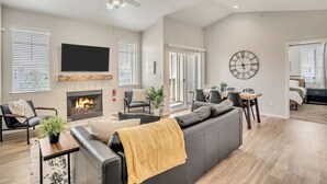 Ein modernes Wohnzimmer mit Kamin, Flachbildfernseher, Deckenventilator und Essbereich mit Tisch und Stühlen.