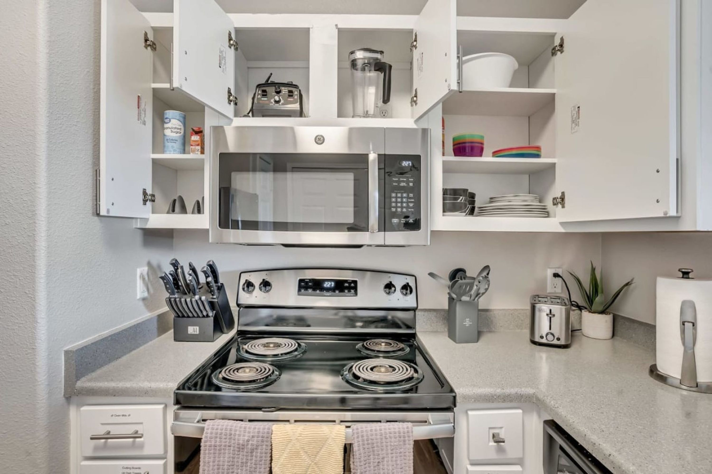 Une cuisine moderne équipée d’une cuisinière, d’un four à micro-ondes et d’un four, tous en acier inoxydable. On trouve des placards au-dessus de la cuisinière et un grille-pain sur le plan de travail.