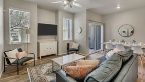 Un salon spacieux doté d’un ventilateur de plafond, d’un téléviseur à écran plat, d’un coin repas avec une table et des chaises, et d’un canapé avec des coussins.