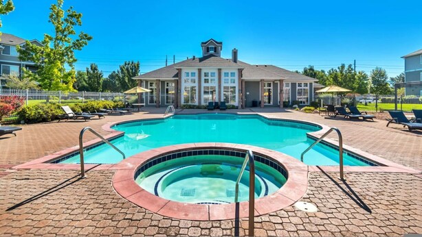 Une piscine avec un jacuzzi, des chaises longues et un bâtiment doté d’une grande fenêtre en arrière-plan.