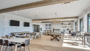 Un interior espacioso y luminoso con techos altos, vigas de madera y una variedad de zonas de estar, incluyendo una mesa de comedor, una barra y un área con sillas y sofá.