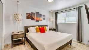 Een slaapkamer met een groot bed, een nachtkastje, een wandlamp en een raam met gordijnen.