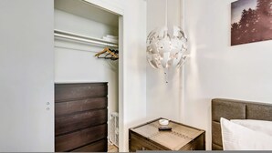 Een slaapkamer met een houten dressoir, een klein tafeltje met een afstandsbediening en een wandlamp.