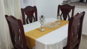 Een eettafel met een witte tafelkleed en een gele loper, omringd door houten stoelen.