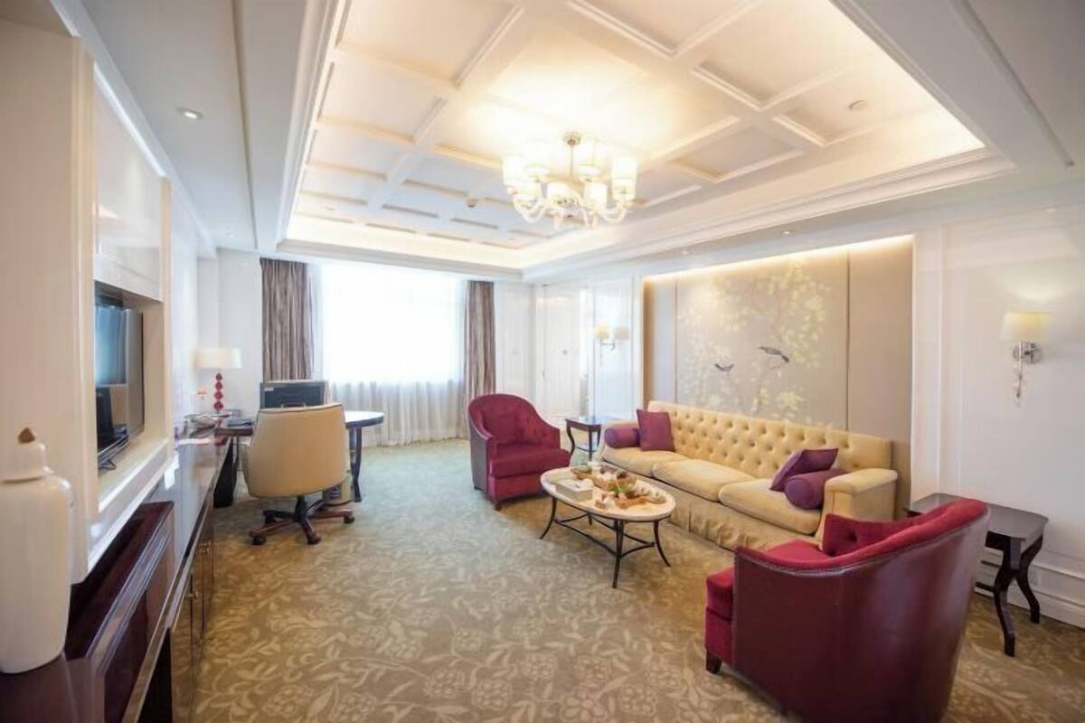 A hotel room with a large bed, a sitting area with a sofa and armchairs, a television, and a desk.