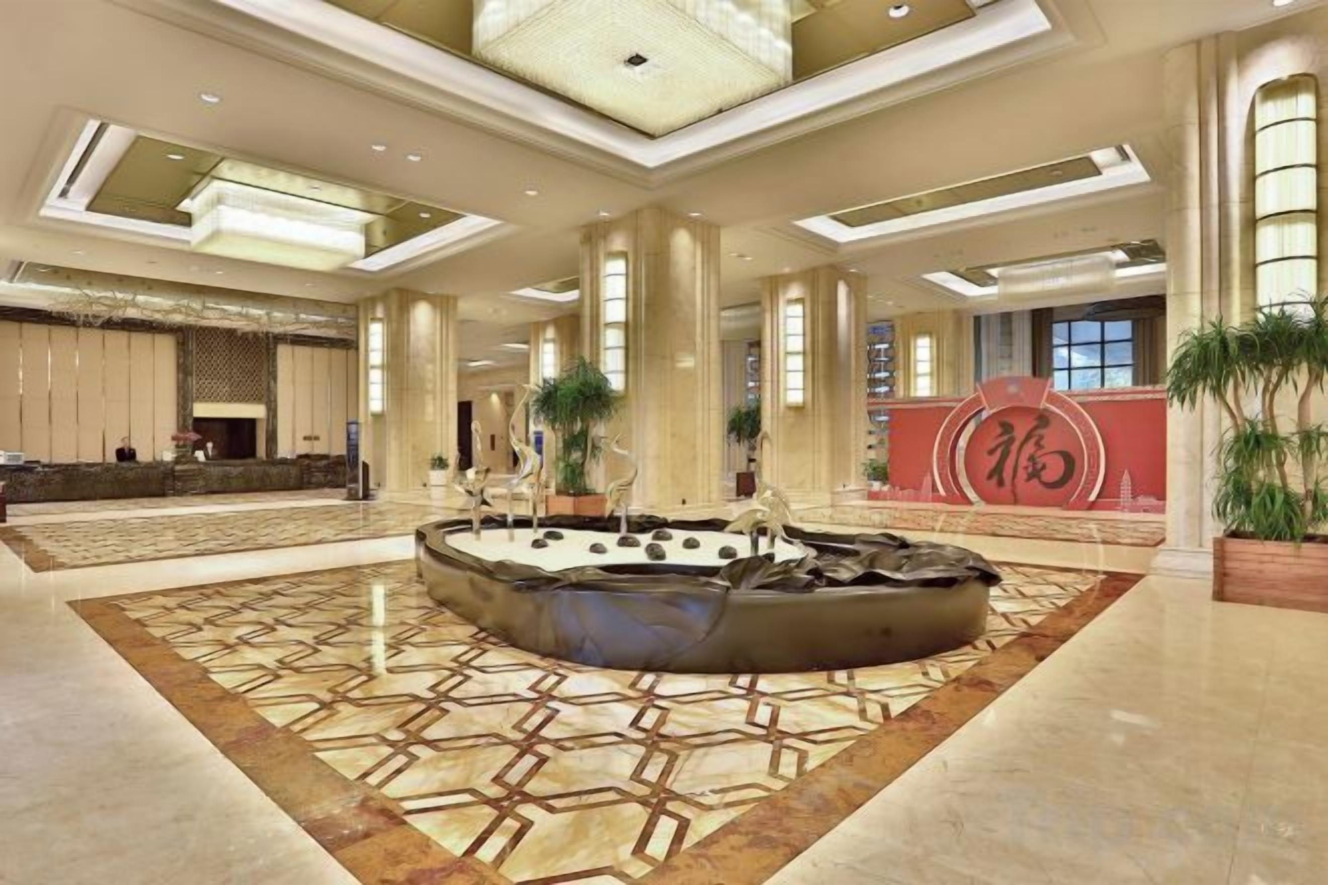 A spacious lobby with a central fountain, a reception desk, and a large decorative wall with Chinese characters.