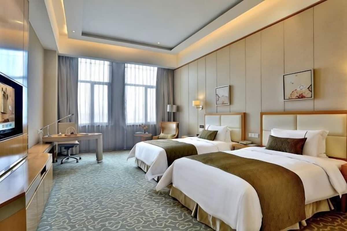 A hotel room with two beds, a desk, a television, and a large window.