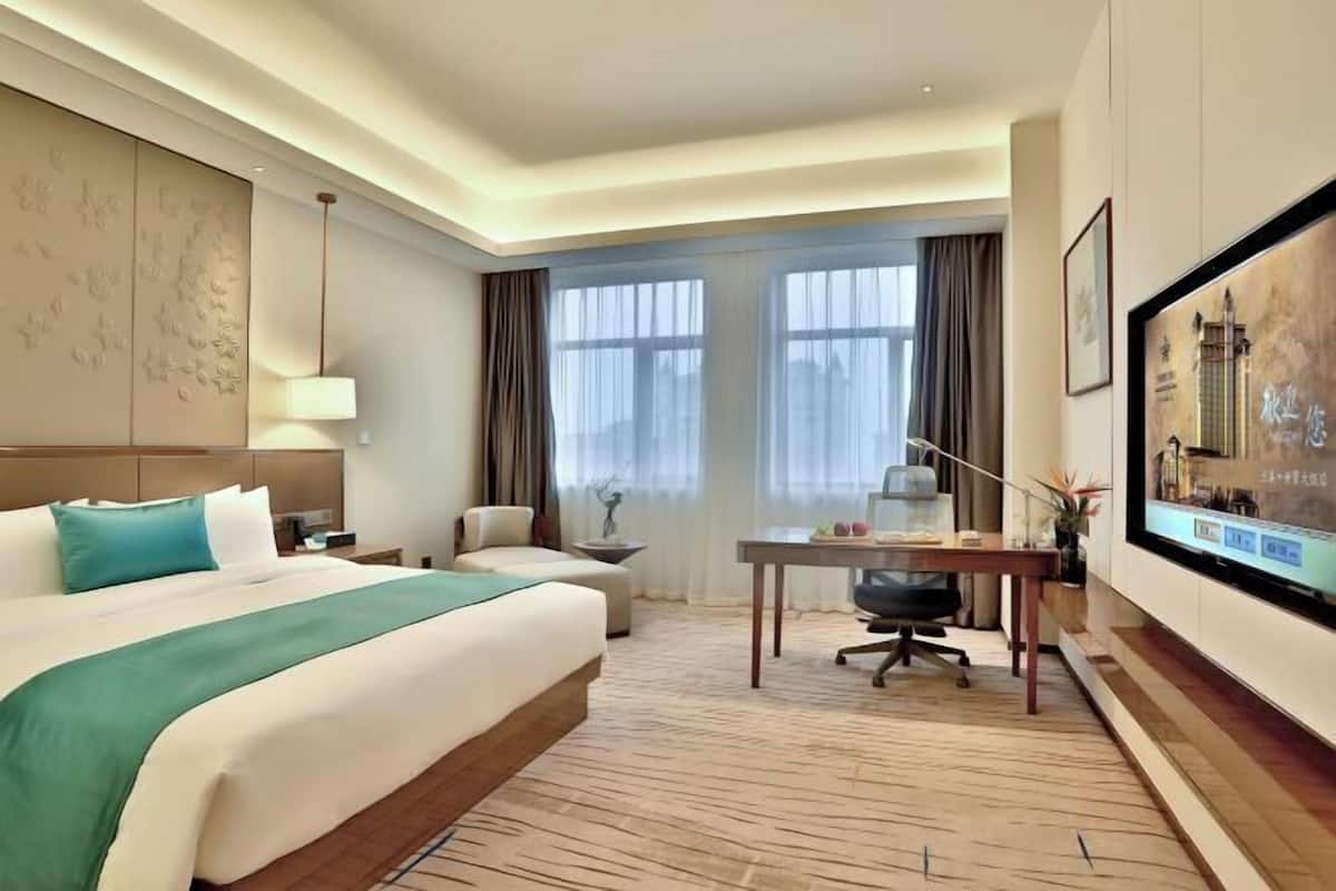 A hotel room with a large bed, a desk, a chair, a TV, and a window with curtains.