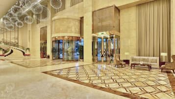 A spacious lobby with a grand staircase, a reception area, and a patterned floor.