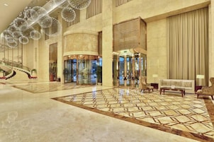 Um hall amplo com uma escadaria imponente, uma área de recepção e piso estampado.