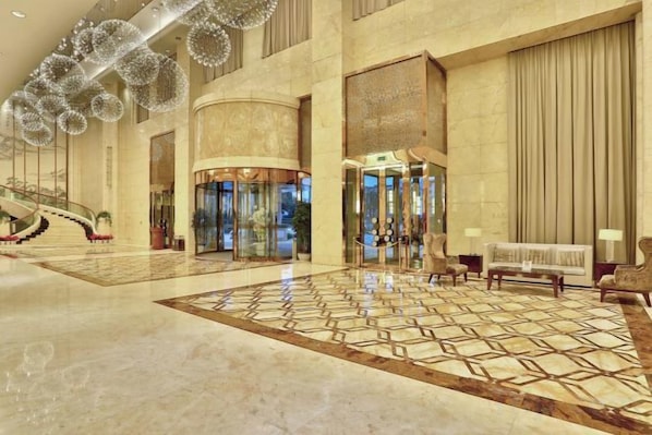A spacious lobby with a grand staircase, a reception area, and a patterned floor.
