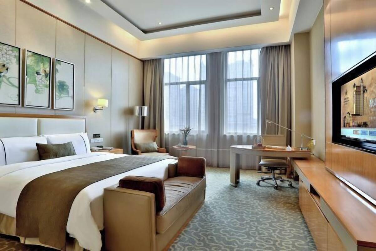 A hotel room with a large bed, a desk, a chair, a television, and artwork on the wall.