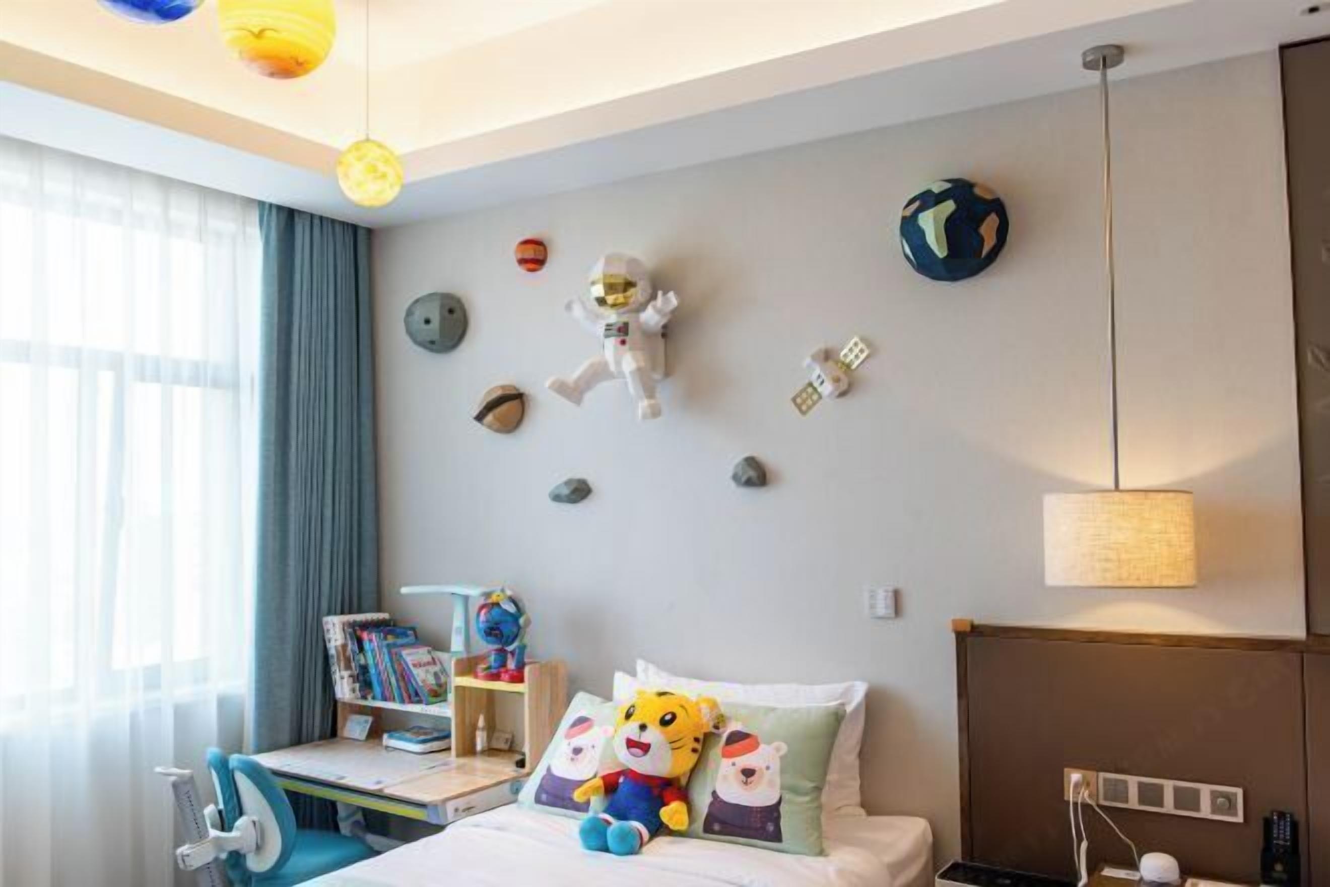 A hotel room with a bed, a desk, and a chair. There are decorative items on the wall, including a plush toy and a globe.