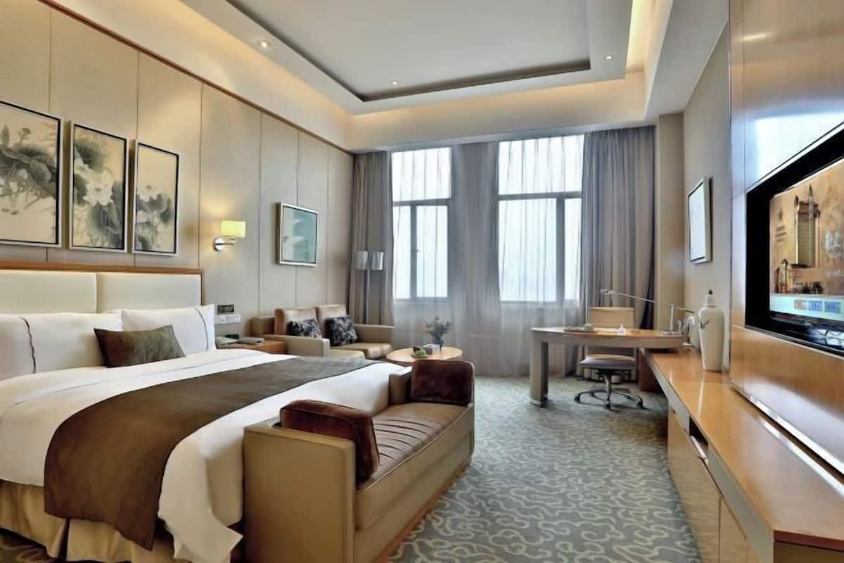 A hotel room with a large bed, a desk, a television, and artwork on the walls.