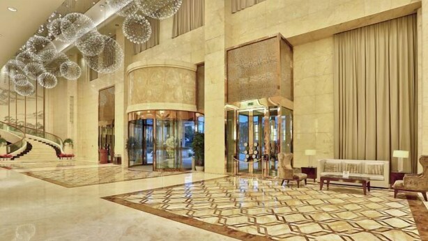 Eine geräumige Lobby mit Marmorboden, einer imposanten Treppe und einem Empfangsbereich mit einer Couch und Sesseln.