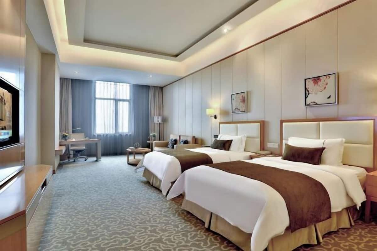 A hotel room with two beds, a desk, a TV, and a large window.