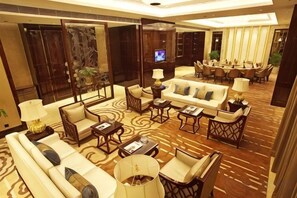 A spacious hotel lobby with a large seating area, a television, and a dining area.