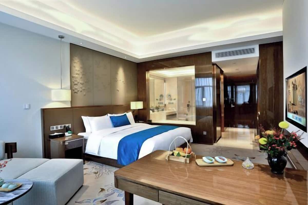 A hotel room with a bed, bedside table, a desk with a chair, a mirror, and a TV.