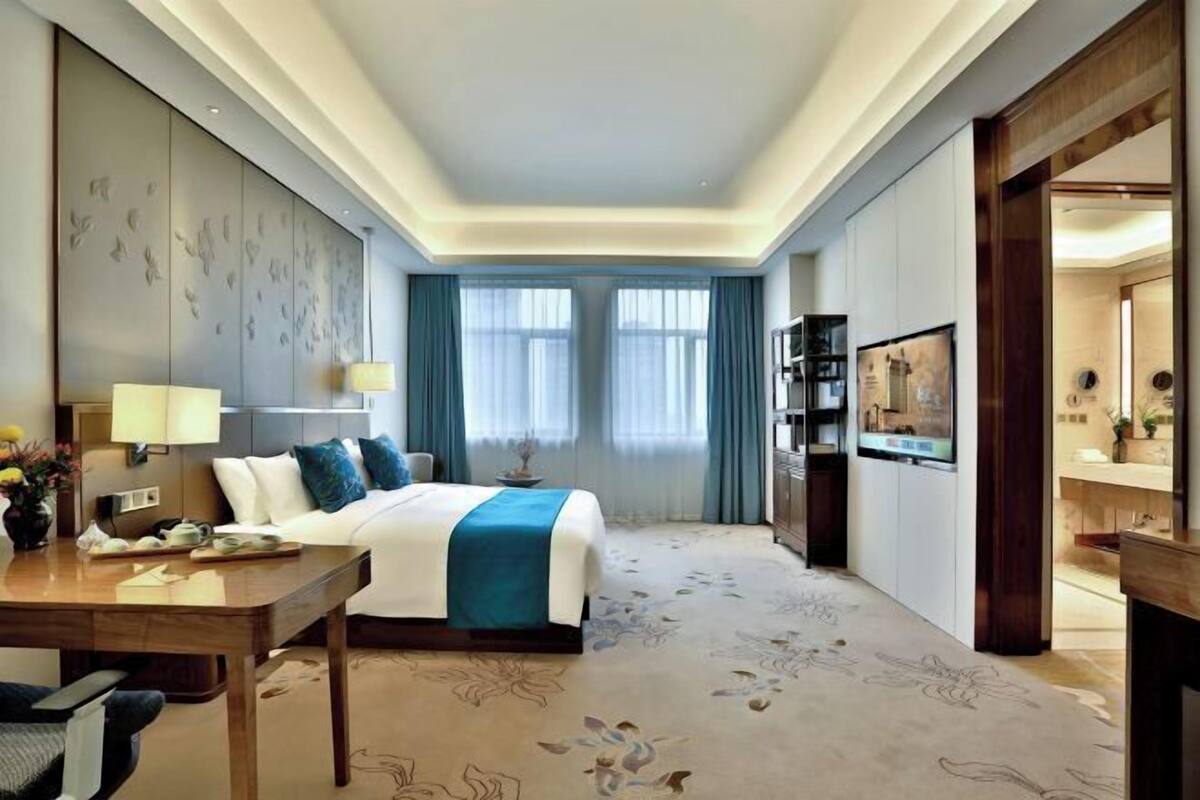 A hotel room with a bed, a desk, a TV, and a bathroom visible through an open door.