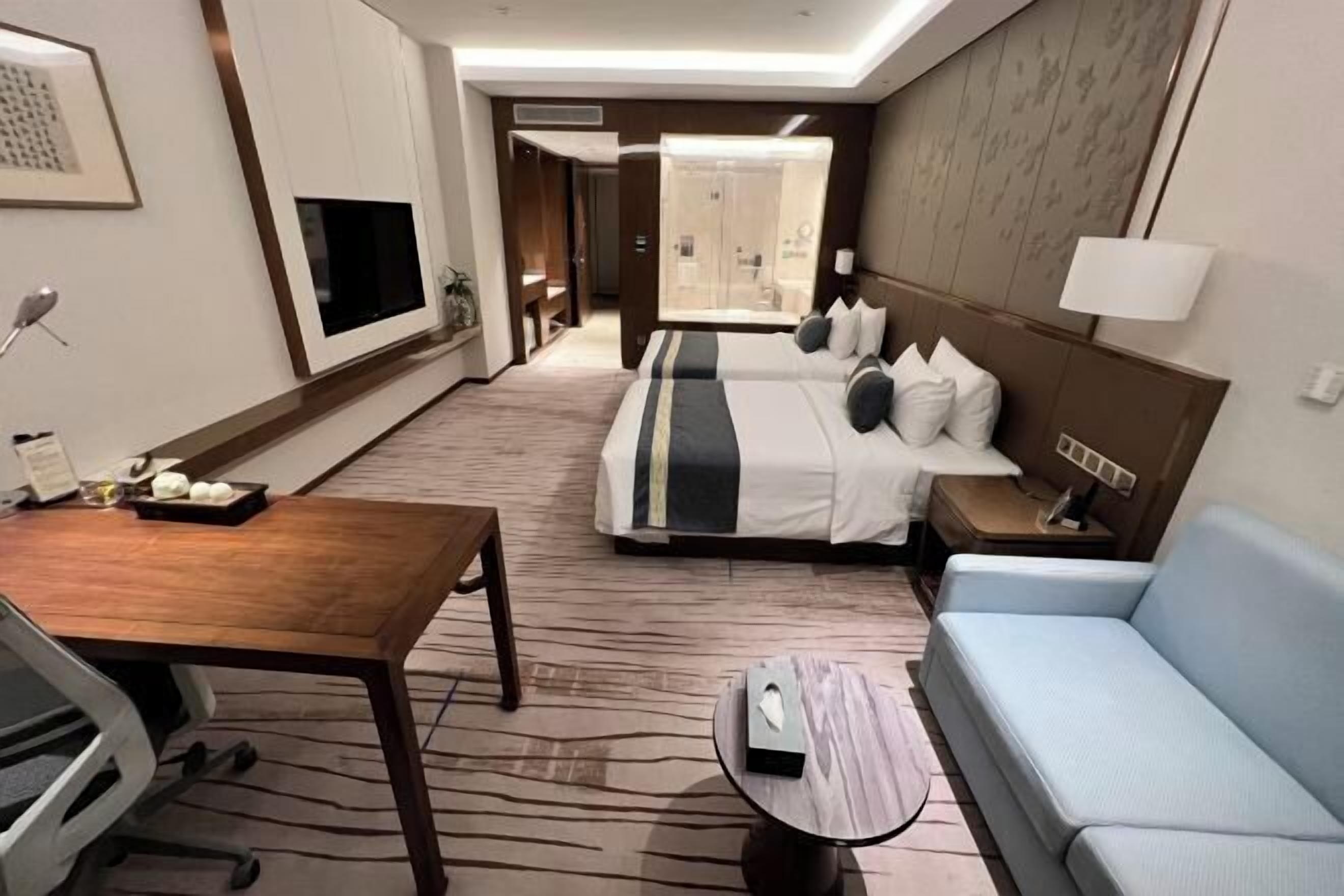 Hotelkamer met een bed, een bank, een bureau, een televisie en een badkamer zichtbaar door een geopende deur.