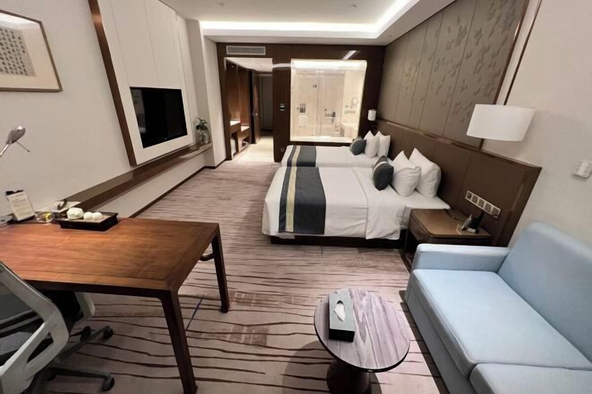 Une chambre d’hôtel avec un lit, un canapé, un bureau, une télévision et une salle de bain visible à travers une porte ouverte.