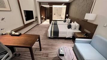 Hotelkamer met een bed, een bank, een bureau, een televisie en een badkamer zichtbaar door een geopende deur.