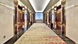 Ein langer, schmaler Hotelkorridor mit Teppichmuster, Marmorwänden und einer Deckenleuchte.