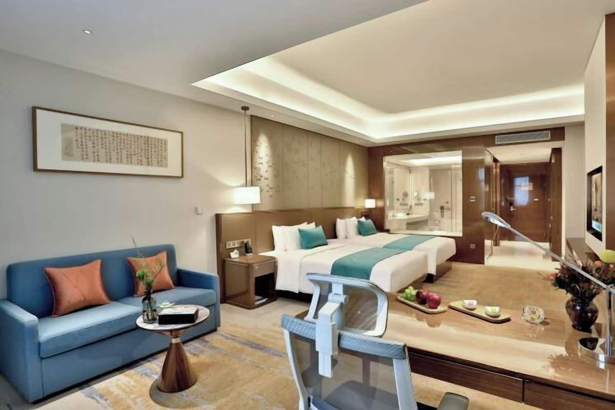 A modern hotel room with a bed, a sofa, a desk, and a mirror.